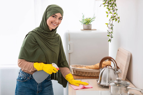 Μουσουλμάνα νεαρή γυναίκα καθαρίζει τραπέζι στην κουζίνα - Φωτογραφία, εικόνα