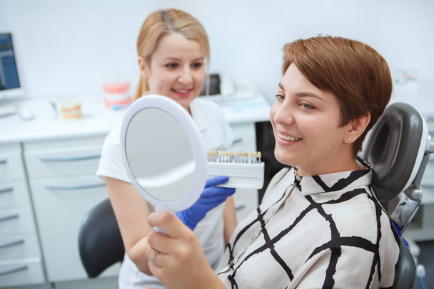 Щаслива молода жінка перевіряє зуби у дзеркалі після відбілювання зубів
 - Фото, зображення