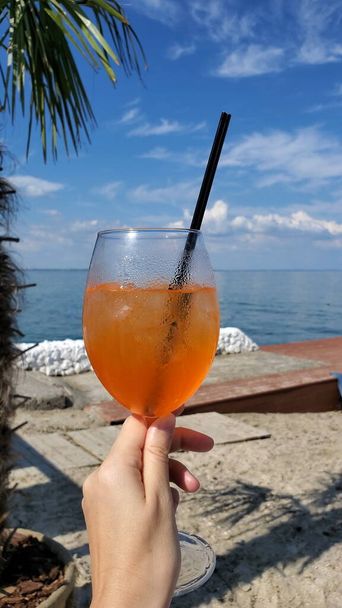 POV zomer cocktail Aperol Spritz in mistig wijnglas met vrouwelijke hand - Foto, afbeelding