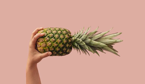 Creative summer vibes idea with a woman's hand holding fresh raw pineapple, pastel bright pink background. Tropical fruit concept, minimalistic aesthetic composition. - Fotoğraf, Görsel