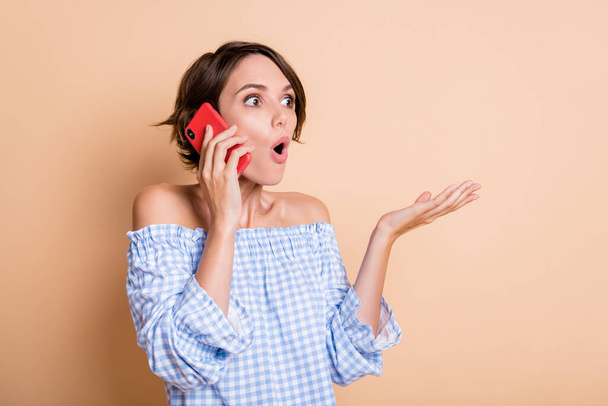 Portrait photo de femme impressionnée parlant au téléphone isolé sur fond beige pastel - Photo, image