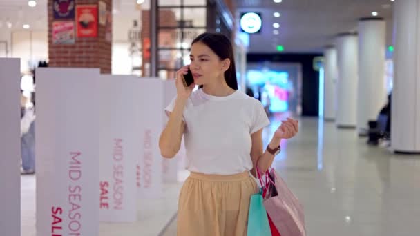 Vrouw praten op mobiele telefoon met vriend tijdens het winkelen dag in winkelcentrum - Video
