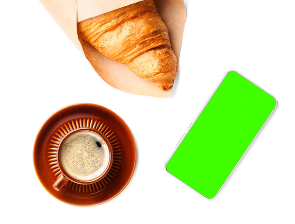 płaski układ brązowy filiżanka czarnej kawy z rogalikiem i telefon zielony ekran - Zdjęcie, obraz