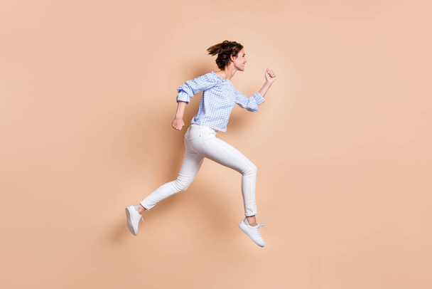 Photo portrait side view of girl running jumping up isolated on pastel beige colored background - Fotoğraf, Görsel