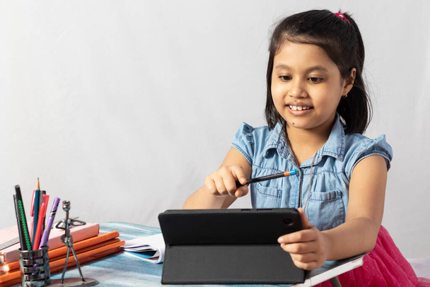 Una bella bambina indiana che frequenta la classe online con tablet su sfondo bianco - Foto, immagini