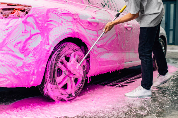 Man worker washes alloy rims of a car at a car wash, a man washes car rims with pink foam and a brush - Valokuva, kuva