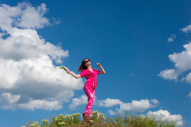 young beautiful girl in pink on a background of clouds in the summer blue sky. - Photo, Image
