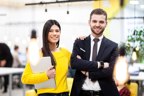 Beautiful Caucasian dark haired girl in yellow posing with businessman wearing suit. Happy colleagues with a laptop in a modern office - Φωτογραφία, εικόνα