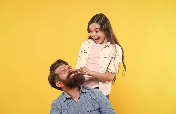 My father is hipster. Little girl pull hipster beard. Happy family yellow background. Hipster barbershop. Barber shop. Hair salon. The bushy beard is great - Zdjęcie, obraz