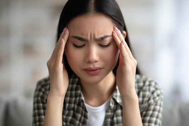 Nahaufnahme einer jungen asiatischen Frau mit Kopfschmerzen, die ihre Schläfen berührt - Foto, Bild