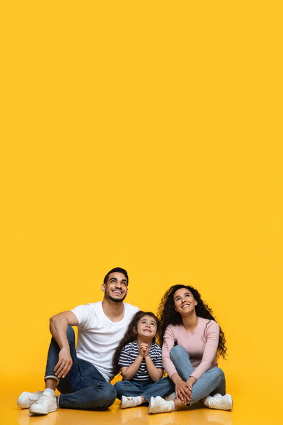 Интересное предложение. Улыбающаяся ближневосточная семья из трех человек смотрит вверх на копировальное пространство - Фото, изображение