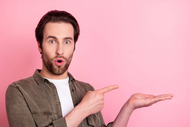 Photo of excited cute young man wear brown shirt pointing finger holding arm empty space isolated pink color background - Fotoğraf, Görsel