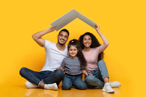 Habitação Familiar. Família árabe feliz de três sentados sob o telhado da caixa - Foto, Imagem