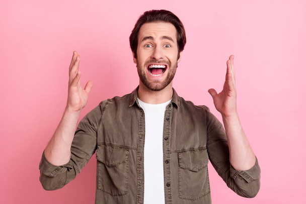 Photo of cute scared young man wear brown shirt pointing screaming rising arms isolated pink color background - Photo, image