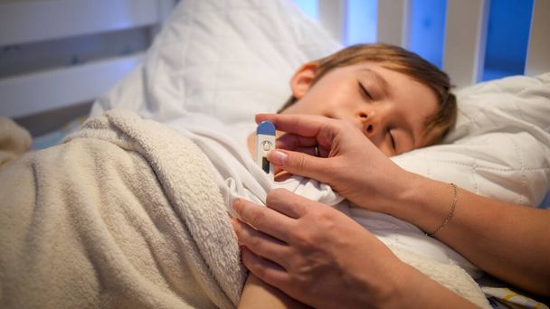 Opiekuńcza matka mierzy temperaturę ciała i głaska śpiącego syna. Pojęcie choroby dzieci, choroby i opieki rodzicielskiej - Zdjęcie, obraz