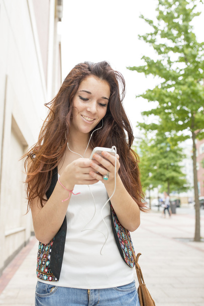 Mujer joven sonriente con auriculares escuchando música, al aire libre
. - Foto, Imagen