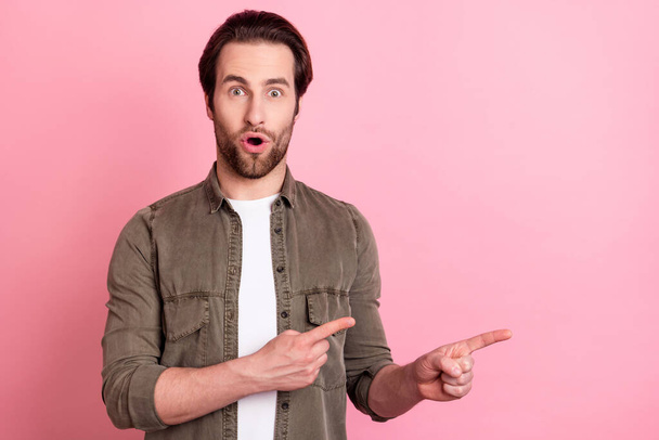 Photo of adorable impressed young man wear brown shirt big eyes pointing fingers empty space isolated pink color background - Foto, afbeelding