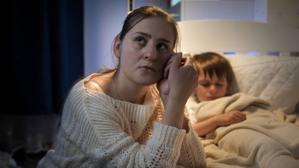 Jovem mulher chorando na cama de seu filho doente à noite - Foto, Imagem