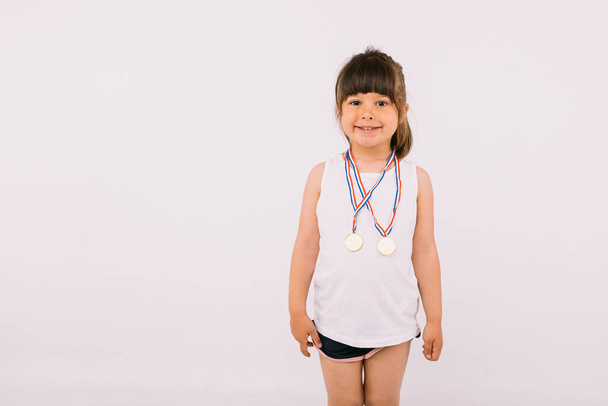 Petite fille aux cheveux foncés avec des médailles de champion sportif. Sport et concept de victoire - Photo, image