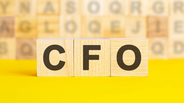 the text CFO is written on wooden cubes on a bright yellow surface. In the background are rows of cubes with different letters. Business concept. CFO - short for chief financial officer - Fotoğraf, Görsel