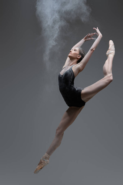 Skilled ballerina dancing leaping against gray background - Photo, Image