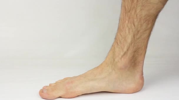 άνθρωπος βάζει στον αστράγαλο βάρη με γυμνό πόδι σε λευκό φόντο, εξοπλισμός για οικιακή άθληση ή προπόνηση ή προπόνηση φυσικής κατάστασης - Πλάνα, βίντεο