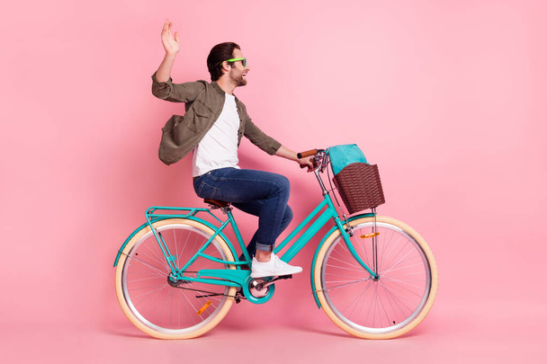Full length profile side photo of young guy happy positive smile ride bicycle wave hand hello isolated over pastel color background - Foto, afbeelding