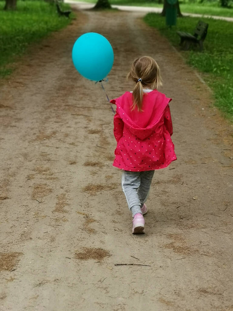 A vertical back view of a female child with a balloon walking in a park - Foto, imagen