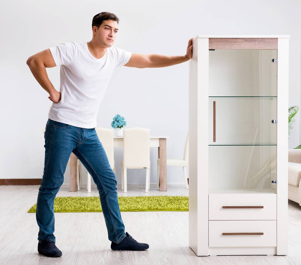 Молодой человек передвигает мебель дома - Фото, изображение