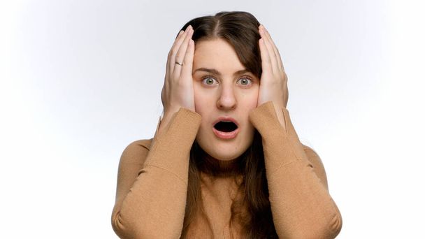 Mujer conmocionada y estresada abre la boca y sostiene la cabeza con las manos. Choque y emociones negativas - Foto, imagen
