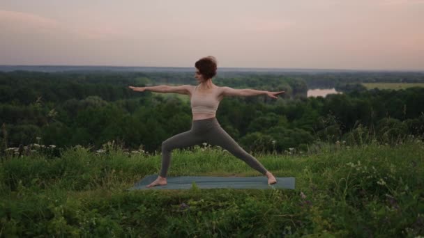 Lassított felvételen egy fiatal nő jóga gyakorlatokat végez egyensúlyozással és nyújtással a tetején. A test és a lélek nyugodt és békés egyensúlya. Testhajlítások és -kanyarok - Felvétel, videó