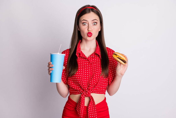 Photo of surprised coquettish girl hold soda cup sandwich send air kiss wear red dotted blouse isolated grey color background - Фото, зображення