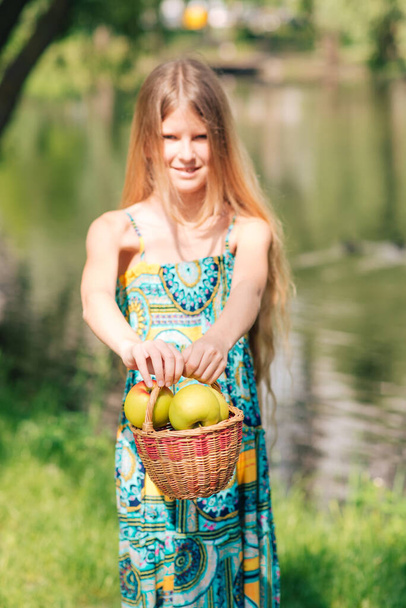 cute young girl with beautiful long hair looks at an apple in her hand.  Summer day. The child collects fruits in the garden. Fresh healthy food for children. Family meals in the summer. - Foto, immagini