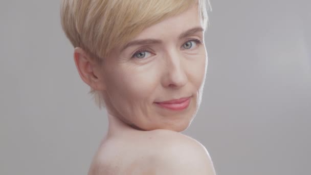 Krásný portrét atraktivní blondýny středního věku s holými rameny dívá do kamery a usmívá - Záběry, video