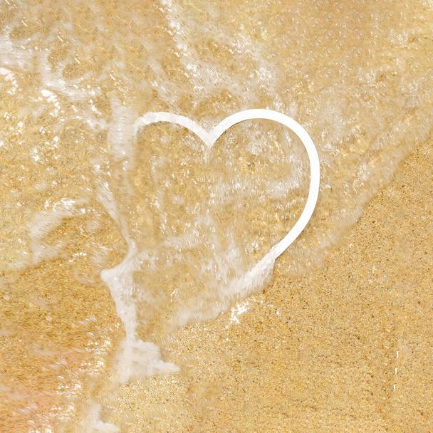 A white frame in a shape of a heart on a sandy beach, half covered by sea foam. Summer love or romantic creative concept - Foto, afbeelding