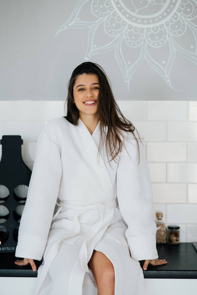 Elegante glimlachende vrouw in witte jas poseren in de keuken - Foto, afbeelding