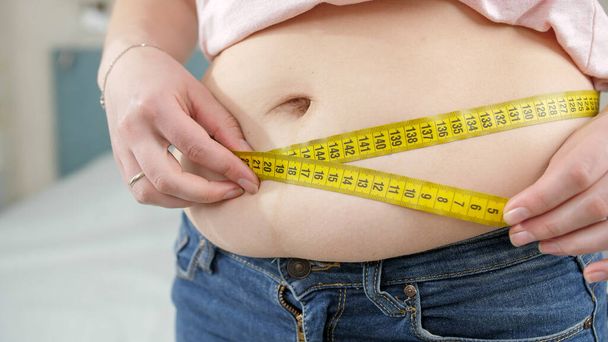 Gros plan de la jeune femme qui perd du poids en mesurant sa taille. Concept de régime, mode de vie malsain, embonpoint et obésité - Photo, image