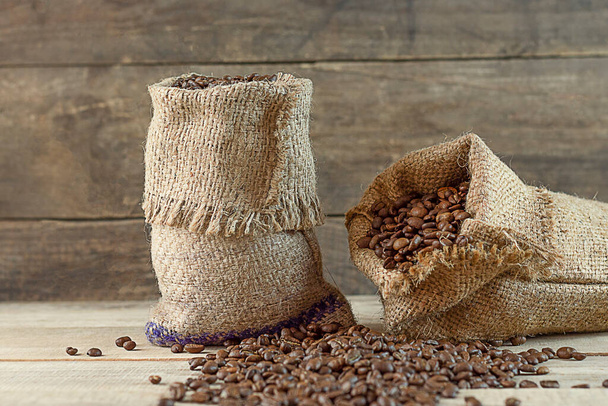 Roasted coffee in two bags on a wooden background. Coffee beans have fallen out into the background.  Coffee business. Harvesting coffee. copyspace - Photo, Image