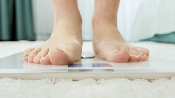Młoda kobieta na bosaka stojąca na wadze cyfrowej, by zmierzyć jej wagę. Pojęcie diety, utraty wagi i zdrowego stylu życia. - Zdjęcie, obraz