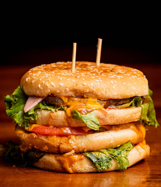 heerlijke en sappige hamburger op een houten tafel op een zwarte achtergrond - Foto, afbeelding