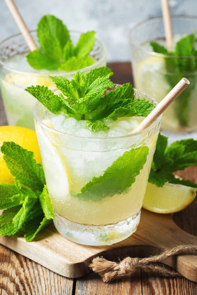 Two glass with lemonade or mojito cocktail with lemon and mint, cold refreshing drink or beverage with ice on rustic blue background - Foto, Imagen