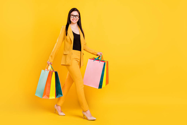 Full size photo of nice millennial young lady hold bags go wear eyewear yellow suit isolated on vivid color background - Photo, image