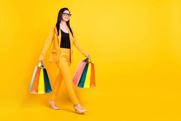 Full size photo of optimistic millennial lady go with bags wear suit shoes isolated on yellow color background - Foto, Imagem