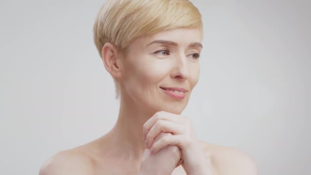 Close up beauty portrait of happy peaceful middle aged woman posing with bare shoulders over grey background - Footage, Video