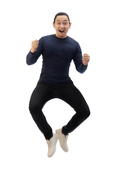 Asian man wearing blue shirt black denim and white shoes, jump while screaming shouting celebrating victory, winning gesture. Full body portrait isolated cut out - Photo, image