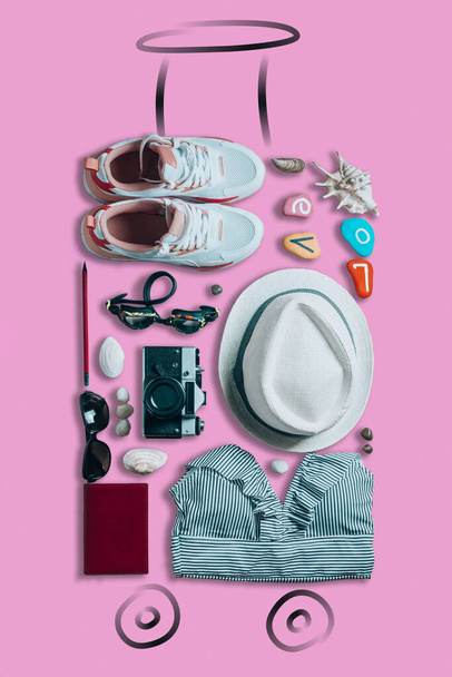 Things laid in form of suitcase with painted wheels and handle on pink background. Travel concept, top view. Vertical - Foto, imagen