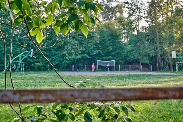 Καλοκαίρι ηλιόλουστη μέρα, τα παιδιά παίζουν ποδόσφαιρο, τον αθλητισμό, το γήπεδο ποδοσφαίρου είναι περιφραγμένο με ένα πλέγμα. - Φωτογραφία, εικόνα