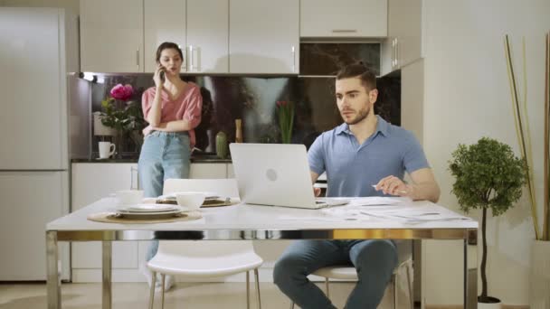 A serious man is working at home and his wife is talking on the phone and distracting him - Footage, Video