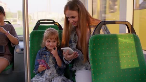 Niña con madre usando la aplicación de red social de Internet de teléfono móvil mientras viaja en autobús - Imágenes, Vídeo