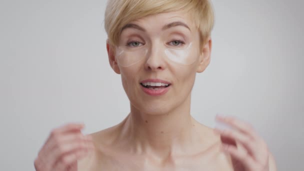 Emocjonalna kobieta w średnim wieku z plamami kolagenu czuje się zdumiona, podnosząc brwi i ręce, szare tło studio - Materiał filmowy, wideo